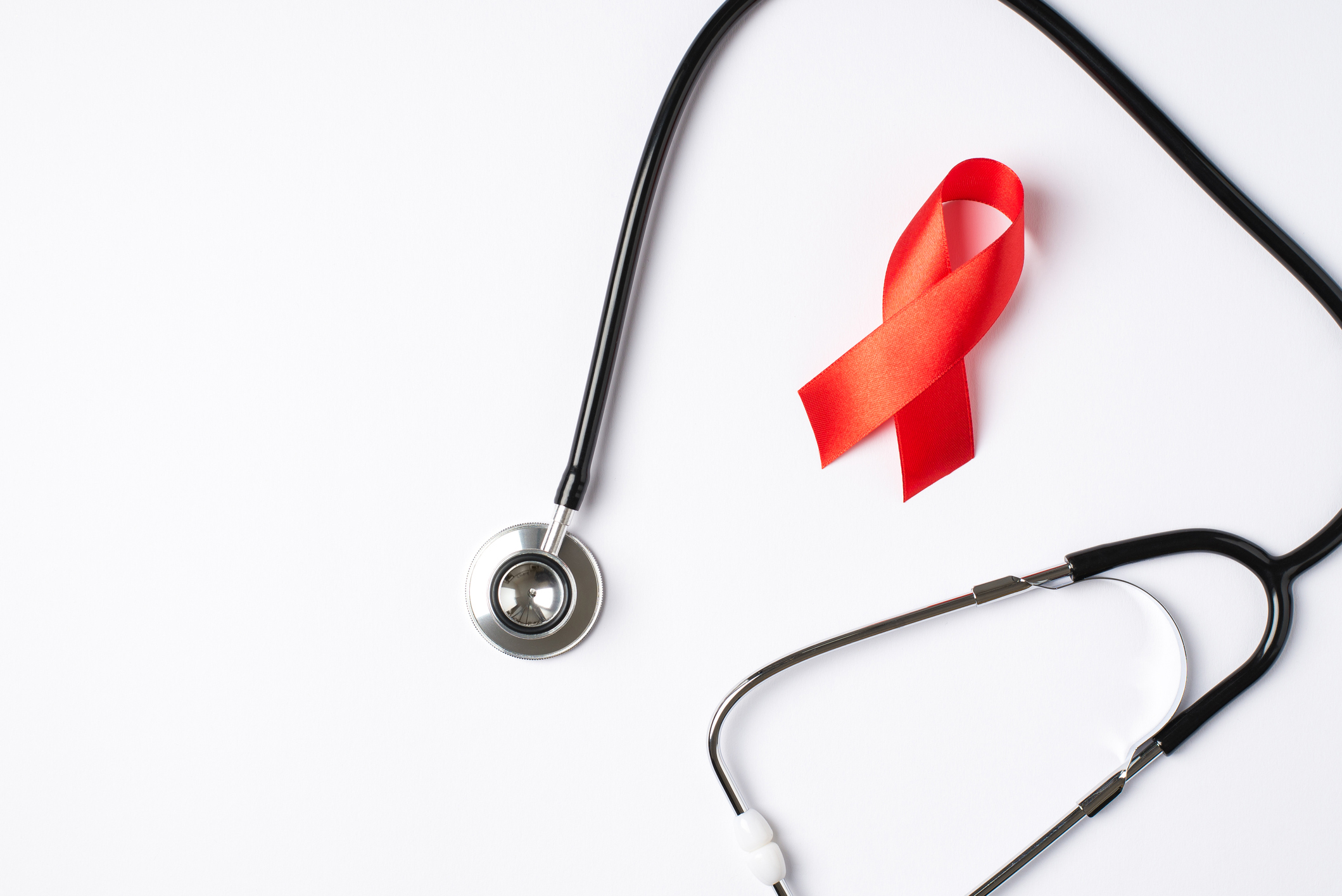 Top view photo of stethoscope and red silk ribbon symbol of aids awareness on isolated white background with copyspace