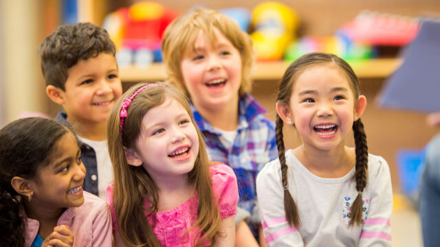 A multi-ethnic group of elementary age children are listening to their teacher read a storybook in class.